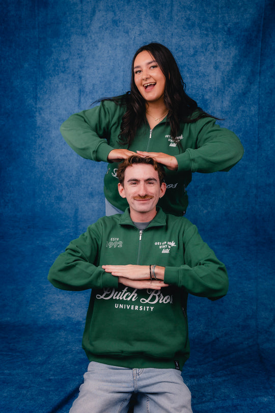 2 people wearing dutch bros green quarter zip against a studio background.