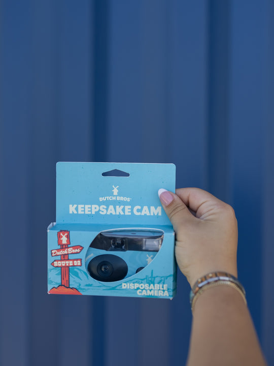 Hand holding a blue packaging of a disposable camera against a blue background