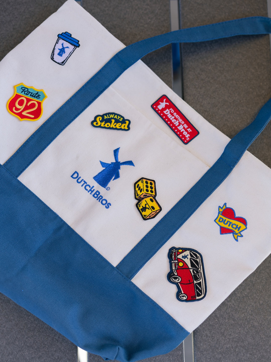 White tote bag with various logos including Dutch Bros on a gray surface