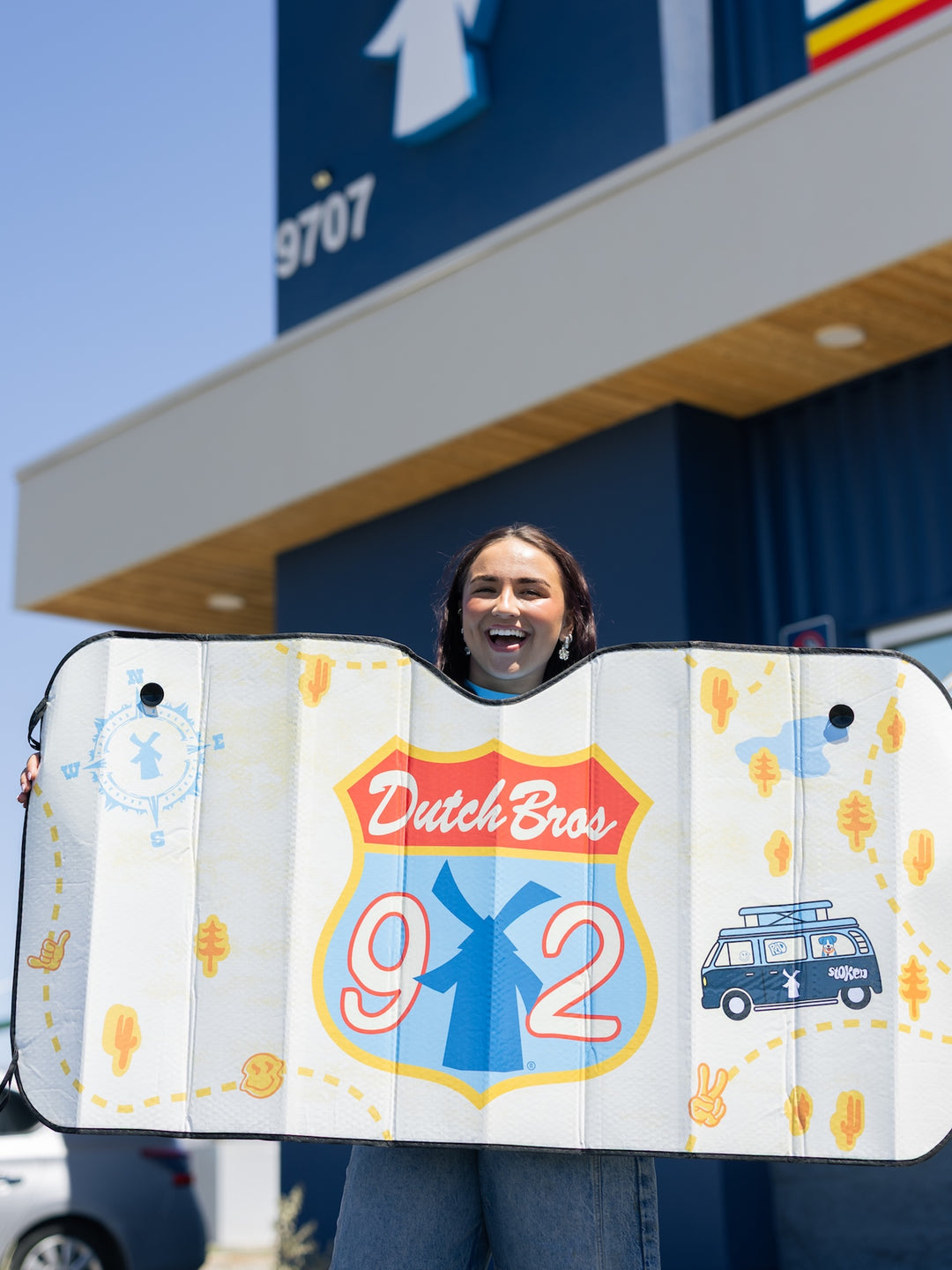 Person holding a Dutch Bros 92 branded sunshade in front of a store.