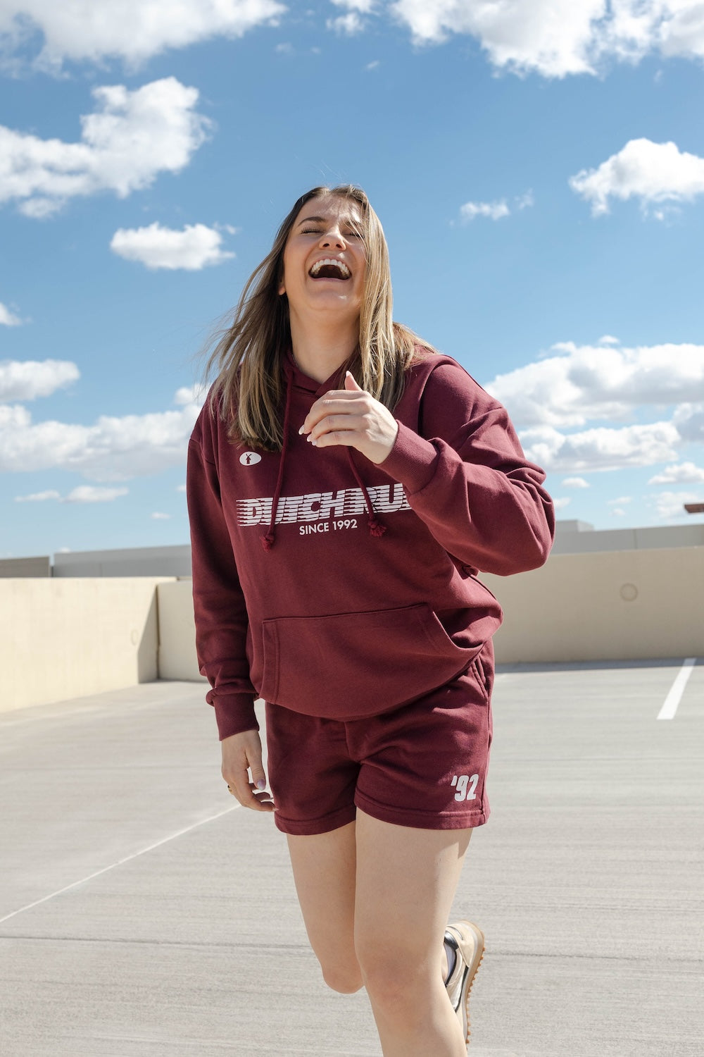 Person wearing a maroon hoodie and shorts with visible branding on a rooftop.