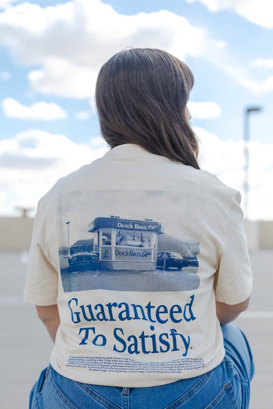 Person wearing a shirt with 'Guaranteed To Satisfy' text and graphic on the back, standing outdoors.