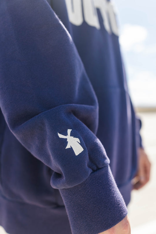 Navy blue sweatshirt with a white logo on the sleeve against a blurred background
